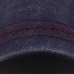Macro du tissu en coton sergé bleu marine avec surpiqûres rouges détaillées sur la casquette