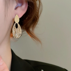 Macro detail of golden oval drop earrings with textured leaf design on model