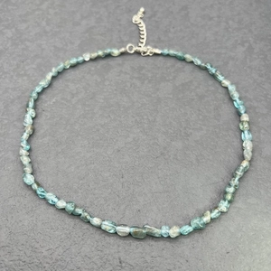 Detail of blue-green natural stone necklace with silver lobster clasp on stone background