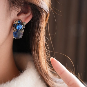 Nahaufnahme von Vintage-Goldohrringen mit blauem Edelstein und Blumendetails am Model