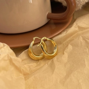 Minimalist thick golden U-shaped hoop earrings on warm textured paper background