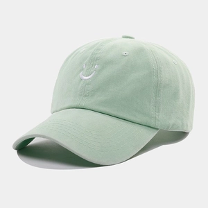 Close-up of white smiling face embroidery on a light green vintage baseball cap