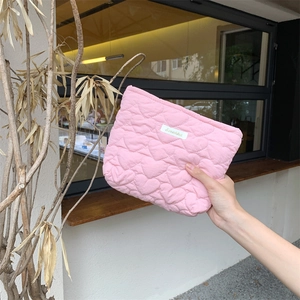 Close-up of pink quilted heart pouch with Sarakku label and zipper being held outdoors