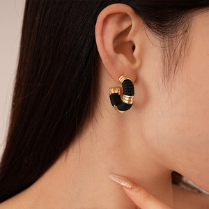 Détail de la boucle d'oreille créole tressée en cuir noir et métal doré en forme de C