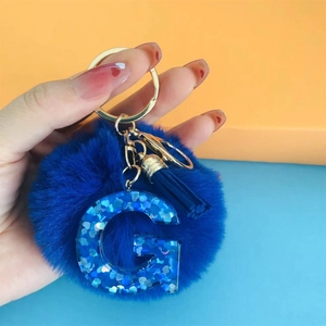 Detail of dark blue pompom keychain with resin letter G pendant and blue tassel ornament