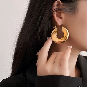 Close-up of chunky gold-plated C-shaped earrings with a polished finish on model