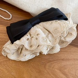 Détail des bords en dentelle brodée et du nœud en satin noir sur la pince à cheveux