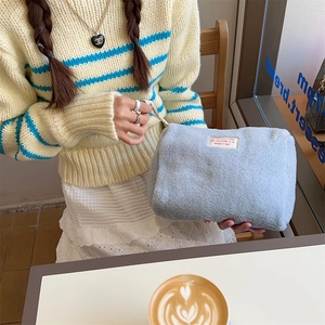 Close-up of soft light blue fleece makeup bag with zipper closure in a cozy cafe setting