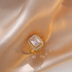 Macro shot of gold rectangle-cut emerald stone ring on silky background with lens flare