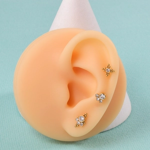 Three gold-plated 16G labret studs with white crystals displayed on a silicone ear model