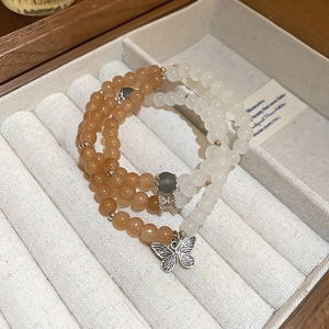 Close-up of double-layer beaded bracelet with orange and white beads and silver butterfly charm