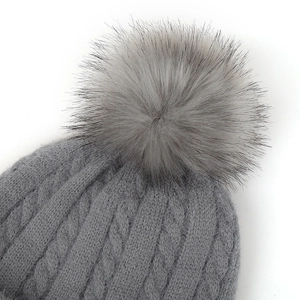 Détail du bonnet gris en maille torsadée avec un grand pompon doux en fausse fourrure