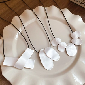 Detail of minimalist geometric pendants on black leather cords over a ceramic plate