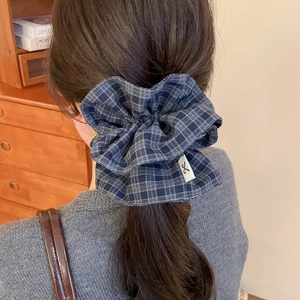Close-up of a blue plaid fabric oversized scrunchie on a model’s low ponytail hair