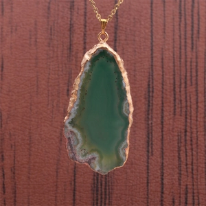 Gros plan du pendentif en tranche d'agate verte avec bords dorés sur chaîne d'or