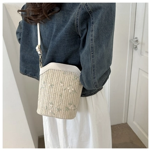 Sac seau en paille brodé porté par un mannequin avec des lanières en cuir blanc