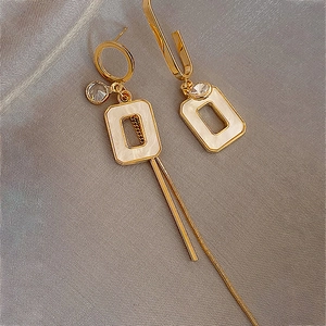 Detail of asymmetric gold tassel earrings with square inserts on silk fabric background