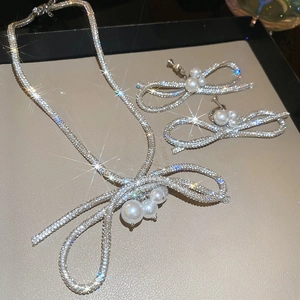 Detailed view of rhinestone bow pendant necklace and matching pearl clip-on earrings set