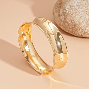 Detailed macro view of a glossy gold metal cuff bracelet with a hinged closure