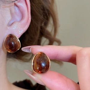 Close-up of amber resin teardrop earrings with gold plating and vintage pleated texture