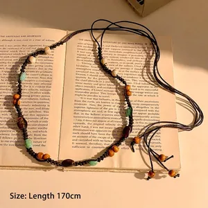 Détail d'une chaîne de taille bohème en perles de bois et conque sur vieux livres