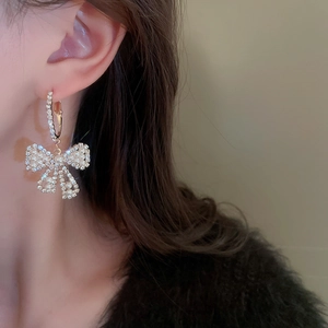 Detail of luxury bow-shaped earrings with pearls and rhinestones on a female model