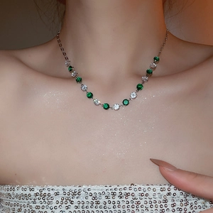 Detail of silver necklace with emerald and clear round-cut zircons worn on model neck