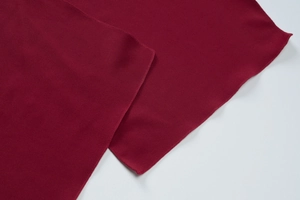 Macro shot of dark red knitted fabric showing refined edge stitching and soft texture