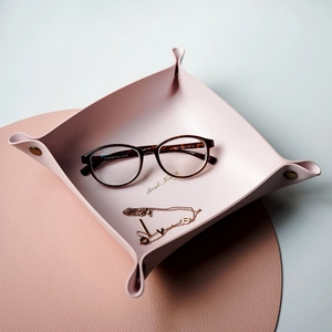 Pink faux leather desk tray with snap buttons holding gold necklace and glasses
