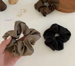 Detailed view of three satin silk scrunchies in neutral colors on a wooden tray