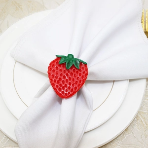 Detailed view of a bright red strawberry napkin ring holding a white cloth napkin on a plate