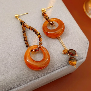 Detail of amber resin tiger eye earrings with gold studs and asymmetrical metal chain drops
