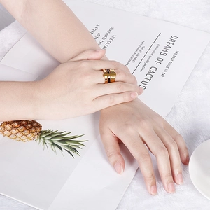 Detail of wide fashion band ring with letter engraving worn on hand over soft white texture