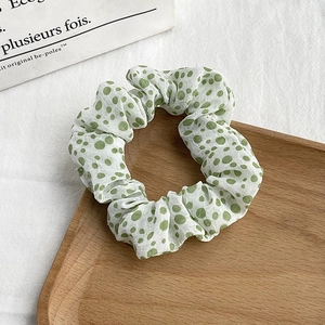 Detail view of floral scrunchie with green polka dots on white chiffon fabric texture