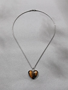 Detail of a heart-shaped tiger eye stone pendant with a silver braided chain necklace