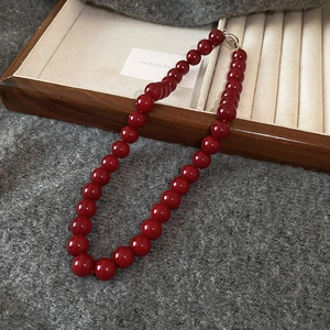 Macro shot of red glass beaded necklace on a wooden tray and grey fabric background