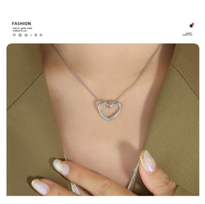 Close-up of a silver heart pendant on a snake chain worn by a model in a green suit