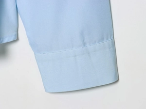Detailed close-up of light blue shirt cuff showing fabric texture and neat stitching