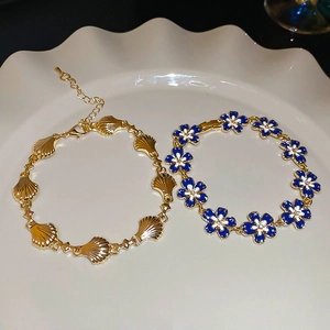 Detail view of a shell-shaped gold bracelet and blue floral enamel bracelet on a ceramic plate