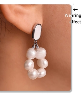 Macro view of baroque pearl drop earrings with hexagonal silver studs worn on the ear