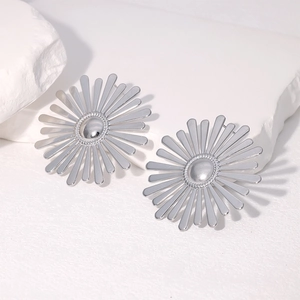 Silver stainless steel sunflower studs displayed on white textured stone surface