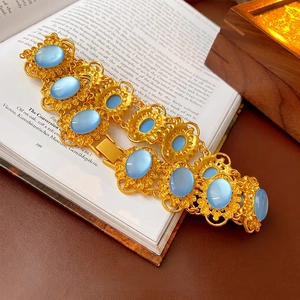 Vintage style gold bracelet with blue cat eye stones on antique book page backdrop