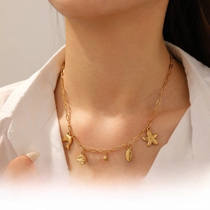 Detail of gold-plated paperclip chain necklace featuring marine life pendants on a model
