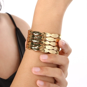 Close-up of golden wide cuff bracelet with textured layered leaf design on a model's wrist