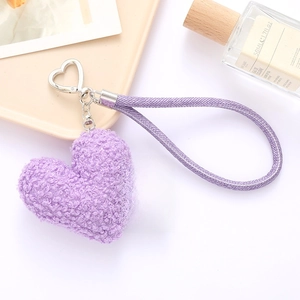 Detail of purple plush heart keychain with metal clasp and fabric strap on a desk