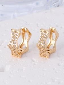 Detailed close-up of gold-plated wavy huggie earrings with shimmering pavé zircon stones