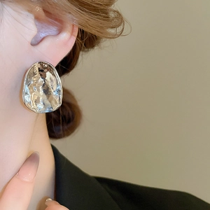 Close-up of irregular silver stud earring with hammered texture on female model ear