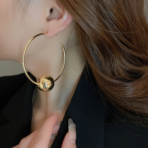 Close-up of a minimalist gold hoop earring with a spherical bead worn by a model