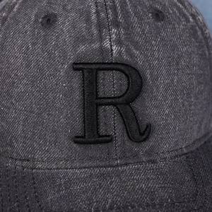 Gros plan de la lettre R brodée noire sur une casquette en jean gris délavé rétro
