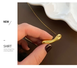 Close-up of a polished golden fluid pendant necklace held between fingers for scale